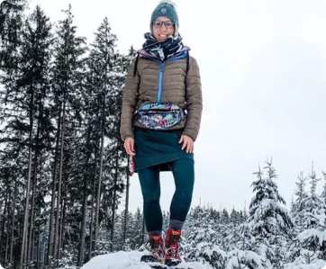 Lächelnde Frau in Winterkleidung auf Schneeberg mit erhobenem Arm