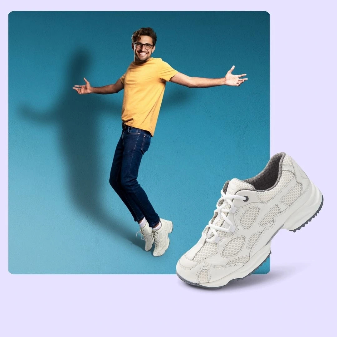 Lächelnder Mann in gelbem T-Shirt und Jeans springt vor blauem Hintergrund. Weißer Freizeitschuh im Vordergrund.