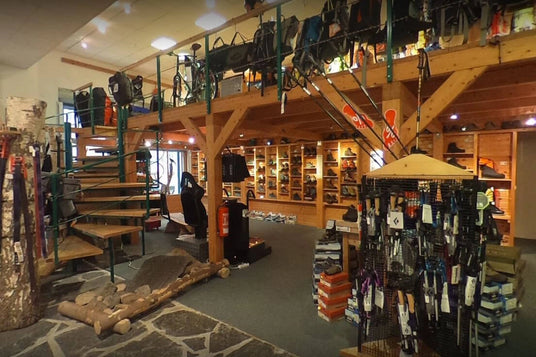 Innenraum eines Outdoor-Geschäfts mit Holzregalen voller Wanderschuhe, Treppenaufgang und diversen Rucksäcken