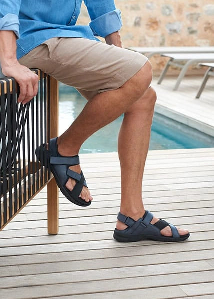 „Mann trägt bequeme Herrensandalen für breite Füße mit verstellbaren Klettverschlüssen auf einer Terrasse.“