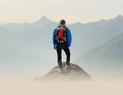 Person auf Bergkamm mit robustem Wanderstiefel, umgeben von Bergen und blauem Himmel. Text: Feel Free
