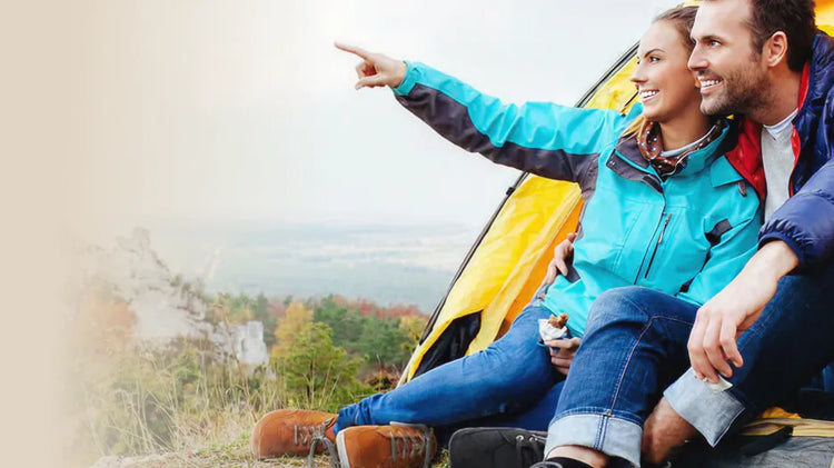 Lächelndes Paar sitzt vor Zelt in den Bergen und blickt in die Ferne. Text: Die Berge rufen! BÄR Wanderschuh Kaufberatung.