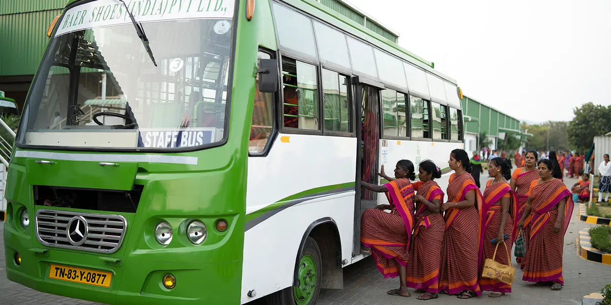 Gruppe von Frauen in traditionellen Saris beim Einsteigen in einen grünen Unternehmensbus vor einer Fabrik