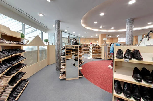 Innenansicht eines modernen Schuhshops mit einer großen Auswahl an Schuhen für Herren und Damen auf Regalen. Elegante Beleuchtung und roter Teppich heben das Ambiente hervor.